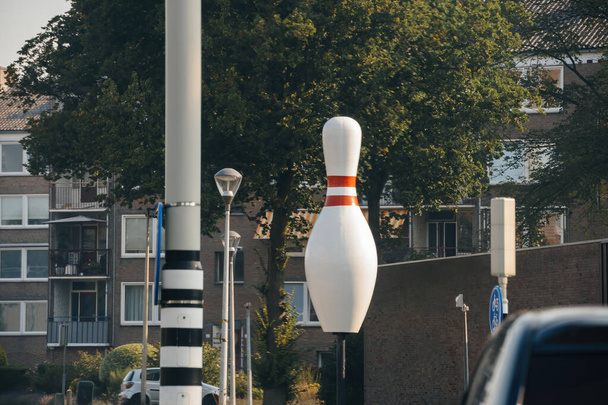 Uma grande escultura de pino de boliche fica proeminente em uma rua na Holanda, cercada por árvores e edifícios residenciais, criando uma cena urbana caprichosa.. - Foto, Imagem