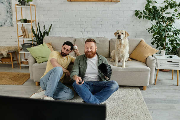 Una coppia gay barbuta si rilassa con il loro Labrador, guardando una partita di baseball nel loro salotto. - Foto, immagini
