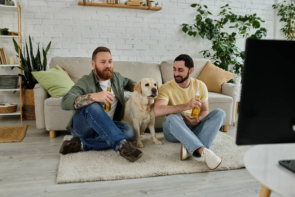 Dos hombres con un perro viendo deportes en un sofá en un acogedor salón juntos. - Foto, imagen