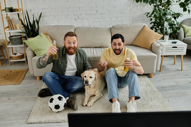 Két szakállas férfi ül együtt a labrador kutyájukkal, sportmeccset néznek a tévében.. - Fotó, kép