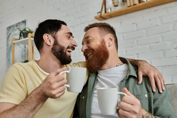 Бородатая гей-пара сидит на диване, наслаждаясь компанией друг друга в своей уютной гостиной. - Фото, изображение