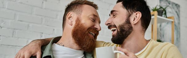 Un couple gay barbu se tient ensemble, exprimant amour et convivialité dans leur salon. - Photo, image