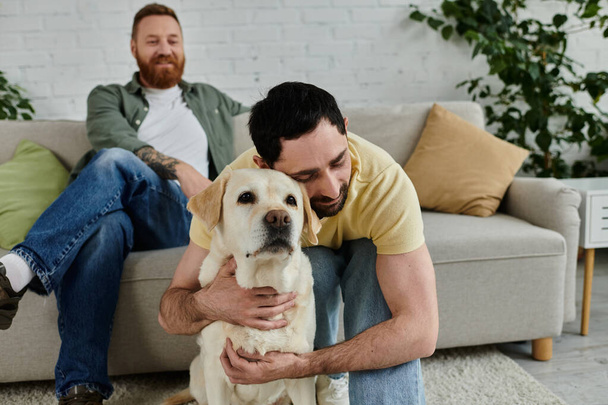 Barbudo gay hombre abrazando labrador en sofá en acogedor salón, compartir el amor y crear recuerdos duraderos. - Foto, Imagen