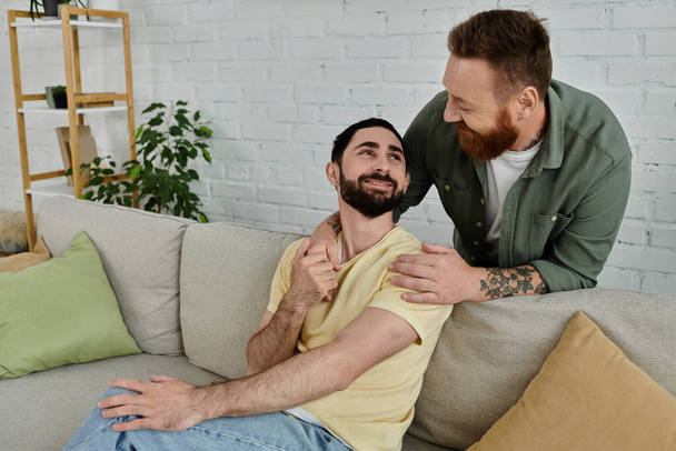 Vousatý homosexuální pár povalující se na moderním gauči, sdílející útulný okamžik se svým labradorem v obývacím pokoji. - Fotografie, Obrázek