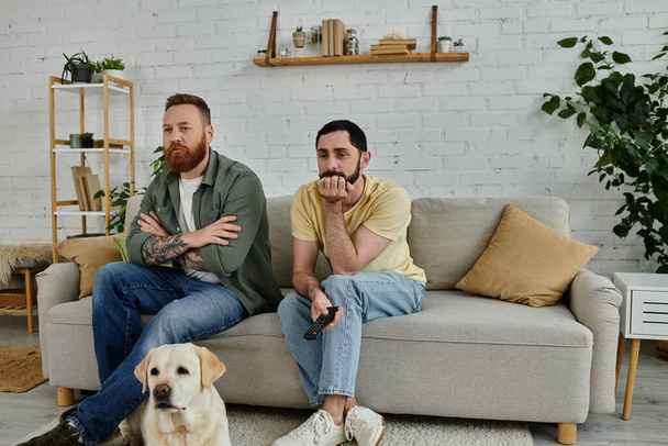 Два человека с бородой сидят на диване, наслаждаясь временем с их Labrador в уютной гостиной. - Фото, изображение