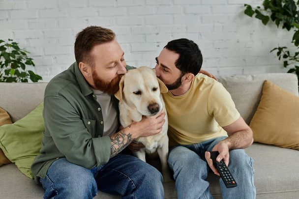 Un hombre barbudo sostiene amorosamente un labrador mientras se relaja en un acogedor sofá en una sala de estar. - Foto, imagen