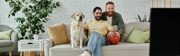 Two men with beards enjoy quality time on couch with friendly labrador in cozy living room. - Photo, Image