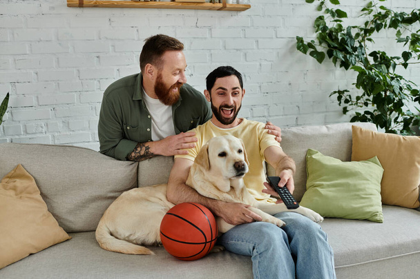 Бородатый мужчина расслабляется на диване рядом с лабрадором, оба наслаждаются качеством жизни в уютной гостиной. - Фото, изображение