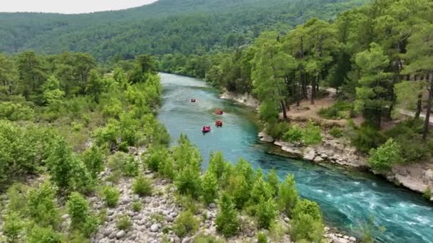 Emberek csoportjai rafting egy türkiz folyó egy buja erdő sziklás part - Felvétel, videó