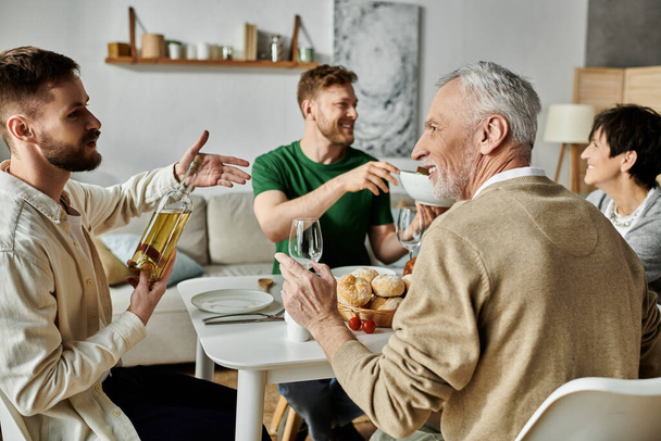 Ένα γκέι ζευγάρι μοιράζεται ένα γεύμα με τους γονείς του στο σπίτι, απολαμβάνοντας μια στιγμή συντροφικότητας και αγάπης. - Φωτογραφία, εικόνα