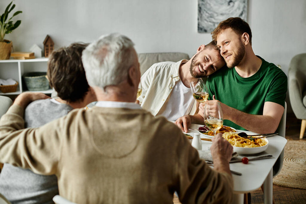 Una coppia gay si siede a un tavolo da pranzo con la loro famiglia, godendo di un pasto e conversazione. - Foto, immagini