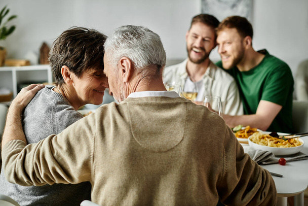 Een gay paar omarmt tijdens een diner met hun familie, presentatie van liefde, acceptatie, en hartverwarmende verbinding. - Foto, afbeelding