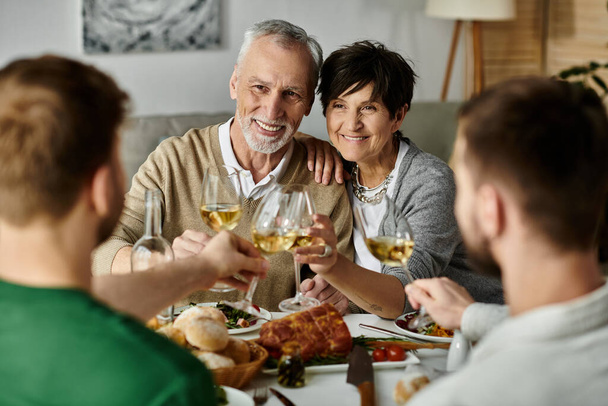 Ένα γκέι ζευγάρι απολαμβάνει ένα γεύμα με τους γονείς του στο σπίτι. - Φωτογραφία, εικόνα