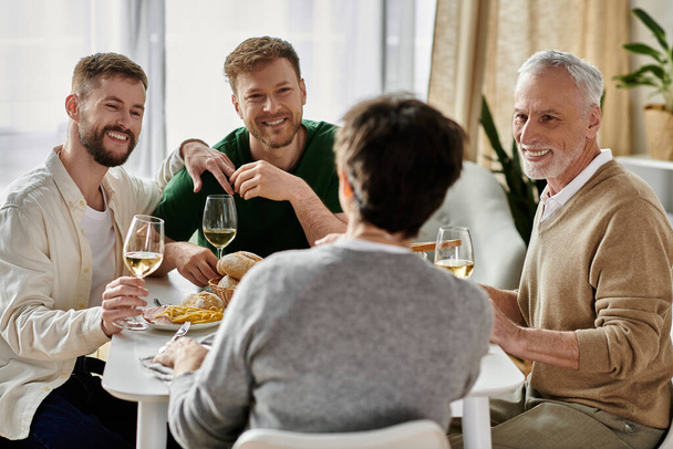 Ένα γκέι ζευγάρι απολαμβάνει ένα δείπνο με τους γονείς του στο σπίτι, μοιράζοντας γέλιο και κρασί. - Φωτογραφία, εικόνα