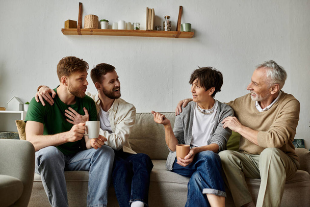 A gay couple sits on a couch with parents, enjoying a conversation and warm drinks. - Фото, изображение