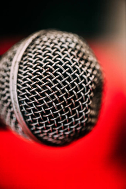 Egy részletes makró felvétel mikrofonokat mutat be bonyolult dróthálóval és textúrával, élénk vörös háttérrel, kiemelve az esti koncertelőadás energiáját.. - Fotó, kép