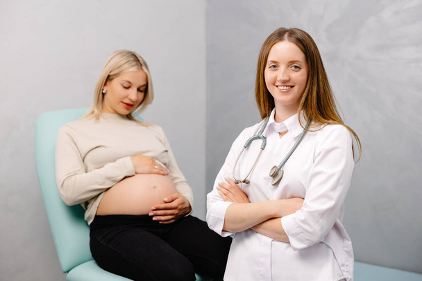 Ginecólogo preparándose para un procedimiento de examen para una mujer embarazada sentada en una silla ginecológica en la oficina y sonriendo. - Foto, imagen