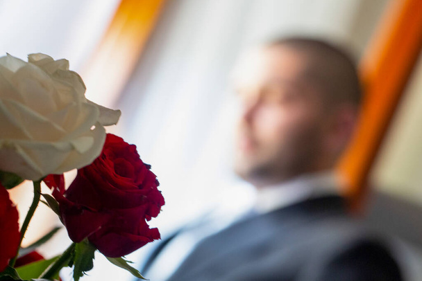 Ένας καλοντυμένος άνδρας κάθεται σε μια καρέκλα με ένα μπουκέτο τριαντάφυλλα μπροστά του, δημιουργώντας μια κομψή και ευχάριστη ατμόσφαιρα - Φωτογραφία, εικόνα