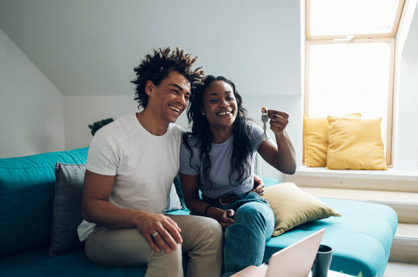 Young african american couple holding home keys in their new apartment after buying real estate. Excited homeowners. - Photo, Image