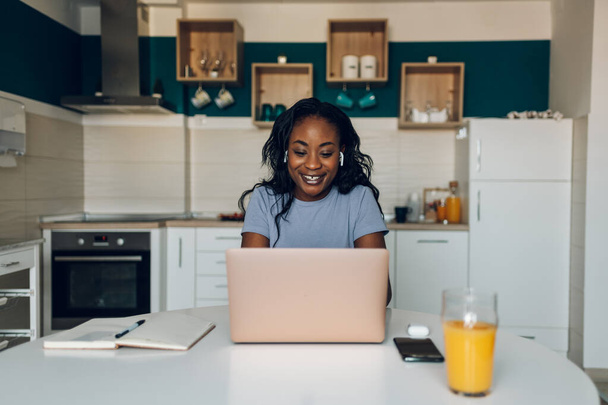 Magnifique jeune femme afro-américaine utilisant un ordinateur portable et payant des factures de location, de gaz et d'électricité en ligne alors qu'elle était dans la cuisine à la maison. Services bancaires en ligne. - Photo, image