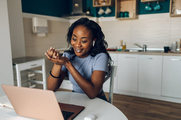 Iloinen afrikkalainen amerikkalainen nainen tekee online-videopuhelun kollegoidensa tai asiakkaidensa kanssa, kun käytät kannettavaa tietokonetta ja työskentelet keittiössä kotona. Jutteleminen verkossa kollegoiden kanssa. Konferenssipuhelu. - Valokuva, kuva