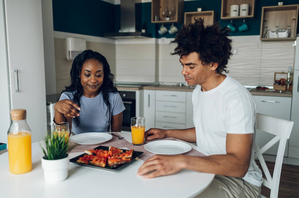 A fiatal afro-amerikai házaspár együtt reggelizik reggel, miközben egészséges ételeket esznek és narancslevet isznak. Romantikus reggel. Ízletes egészséges étel.. - Fotó, kép