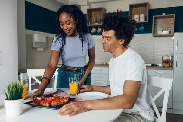 Adoro la coppia afroamericana che fa colazione in cucina a casa e beve succo d'arancia. Famiglia afroamericana di due persone. - Foto, immagini