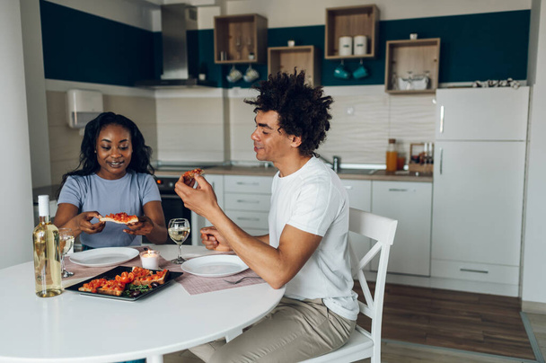 Felice coppia afroamericana bere vino bianco e godersi la cena insieme mentre in cucina a casa. Data a casa. - Foto, immagini