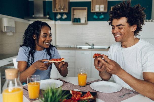 若いアフリカ系アメリカ人のカップルは,健康的な食べ物やオレンジジュースを食べながら朝食を共にする. ロマンチックな朝. 美味しい健康食品. - 写真・画像