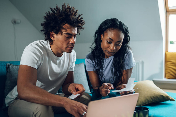 Afro-Amerikaans echtpaar doen hun rekeningen thuis en met behulp van een laptop en een creditcard voor online betalen. Online winkelen en kopen. Facturen en gezinsbudget. - Foto, afbeelding