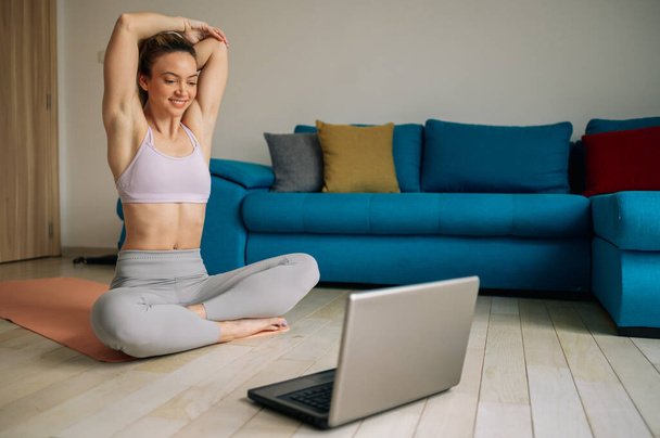Jeune femme sportive s'entraînant à la maison et répétant des exercices tout en regardant une séance d'entraînement en ligne sur un ordinateur portable. Mode de vie sain. - Photo, image