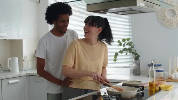Medio tiro de joven negro besar novia freír huevos para su desayuno en casa cocina - Metraje, vídeo
