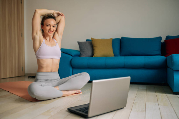 Blogerka fitness nagrywa wideo na swoim laptopie i trenuje w domu w salonie. Koncepcja sportu i rekreacji wpływającej na styl życia. - Zdjęcie, obraz