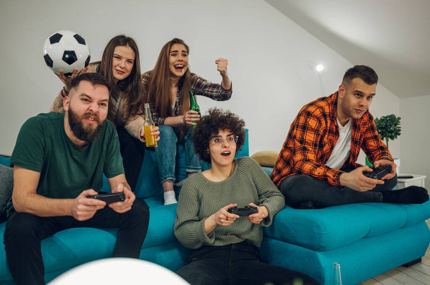 Grupo de amigos jugando videojuegos en casa. Jugar videojuego con joysticks. Amistad, tecnología y concepto de juegos. - Foto, imagen