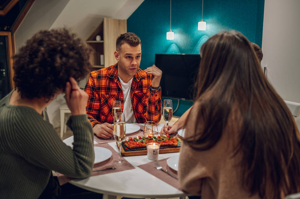 Group of cheerful young people enjoying dinner while sitting at the kitchen table together. Having a great time with friends during dinner while drinking and having fun. - Foto, Imagem