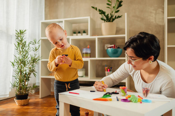 Äiti ja lapsi poika leikkivät värikkäällä savella kotona ja maalaavat yhdessä. Lapsenvahti nainen tai täti auttaa lapsi poika samalla hauskaa. Onnellinen perhe. Opetuspelit lapsen kehitykseen - Valokuva, kuva