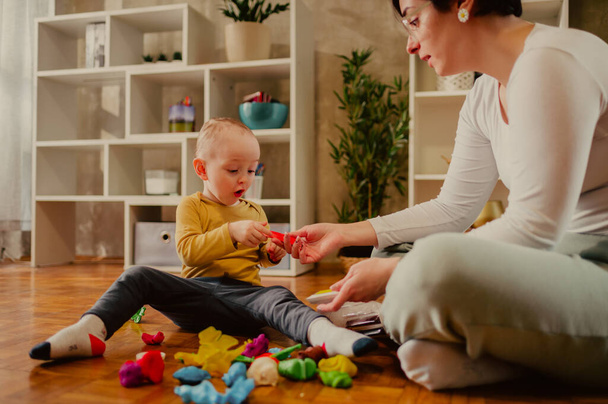 Family of two creating fun objects with clay and improving fine motor skill trough the games. Toddler boy playing with his mother or aunt. Funny educational games for children concept. Focus on a boy. - Photo, Image