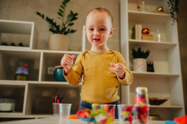 Portret uroczego dziecka bawiącego się kolorową gliną. Mały chłopiec tworząc obiekty i kształty podczas formowania gliny lub plastycyny. Gra edukacyjna dla dziecka i malucha. Przestrzeń kopiowania. - Zdjęcie, obraz