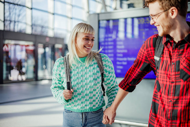Young hipster couple is holding hands and going on a train at metro station. A young passenger is leading his girlfriend on train station while going on a train. Happy travelers at metro station. - Photo, Image