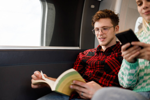 Portret van een man die pendelt naar het werk per trein of metro terwijl hij een boek leest. Hipster studeert voor zijn examen op weg naar school. Mensen reizen vervoer concept. Kopieerruimte, - Foto, afbeelding