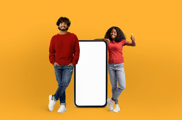 A man and a woman are standing next to a blank screen, both posing as if they are presenting something. The blank screen offers a versatile space for text or images. - Photo, Image