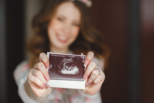 Closeup of a pregnant woman with an ultrasound picture in her hands. - Foto, imagen