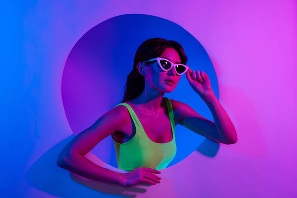 Фото женщины касаются солнцезащитные очки взгляд пустое пространство из круга отверстие изолированный светящийся неоновый фон. - Фото, изображение