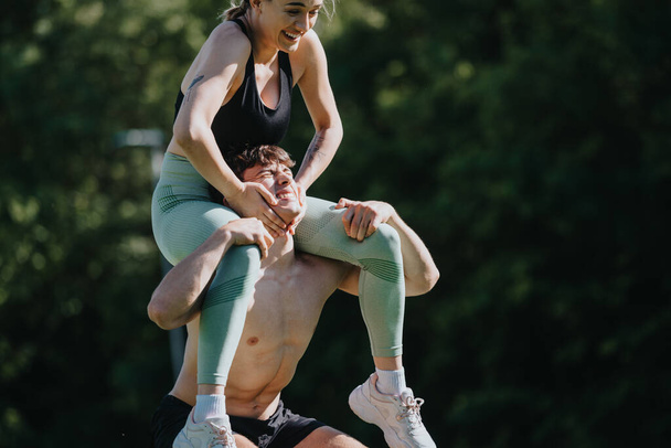 Атлетическая пара, занимающаяся веселыми и игривыми упражнениями во время тренировки на открытом воздухе в солнечном парке, способствуя фитнесу, радости и здоровому образу жизни. - Фото, изображение
