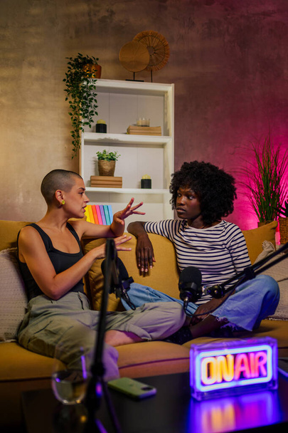 Porträt einer vielseitigen Radiomoderatorin, die ein interessantes Gespräch über eine Audio-Sendung in einem Studio führt. Zwei multirassische Frauen nehmen einen Internet-Podcast für ihren Social-Media-Kanal auf. - Foto, Bild