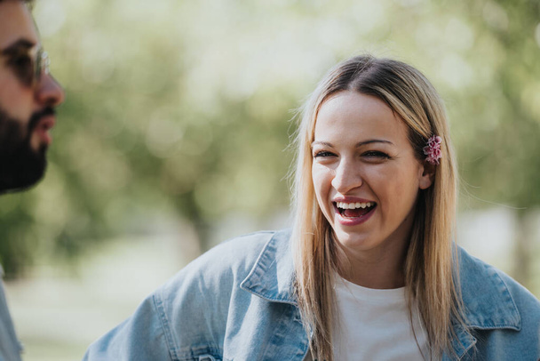 Un moment franc capture une jeune femme riant chaleureusement à côté d'un ami masculin dans un parc ensoleillé, incarnant la joie insouciante et le style décontracté. - Photo, image