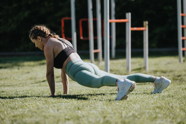 Mujer joven realizando un ejercicio de tablón en un parque, centrándose en la aptitud y la salud durante una sesión de entrenamiento al aire libre. - Foto, Imagen