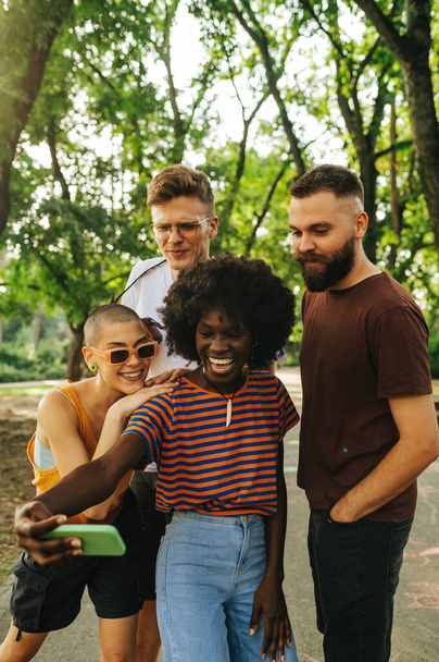 Jeunes personnes interraciales prenant des selfies dans la nature et célébrant l'unité et la vie. Une afro-américaine prend des selfies pendant que ses amis hippies posent et sourient au téléphone. Diversité, unité. - Photo, image