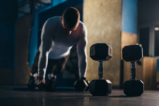 Shot of a young man doing push ups on a dumbbells in the gym - Photo, Image