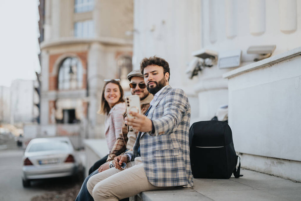 Eine Gruppe junger Unternehmer, die bei einem zwanglosen Geschäftstreffen im Freien mit einem Smartphone in einer städtischen Gegend zusammenarbeiten. - Foto, Bild